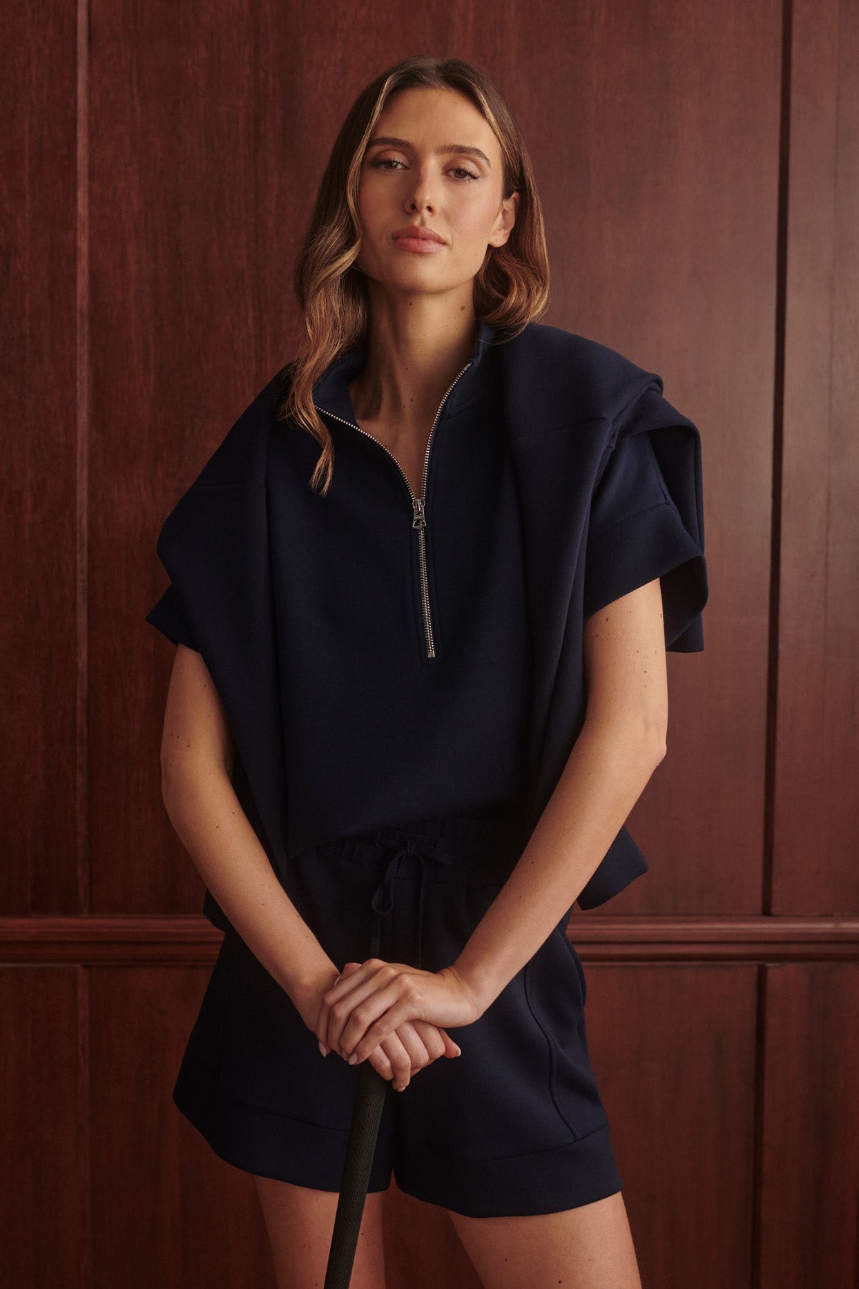 Woman wearing a navy blue outfit against a wooden paneled wall