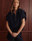 Woman wearing a navy blue outfit against a wooden paneled wall