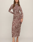 A woman modeling a long-sleeve high-neck midi dress with a brown and beige zebra print, paired with clear high-heeled sandals, against a solid light beige studio background.