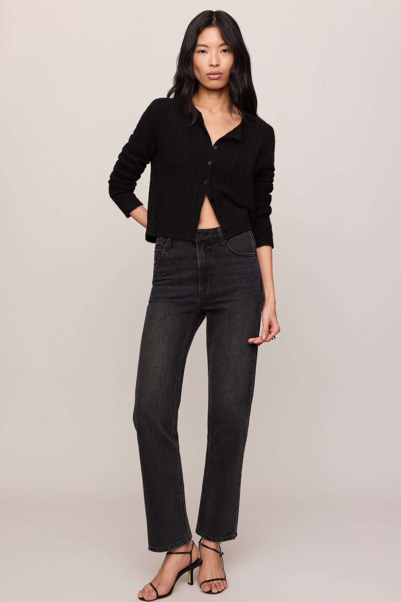 Woman wearing a black button-up shirt and dark jeans against a plain background