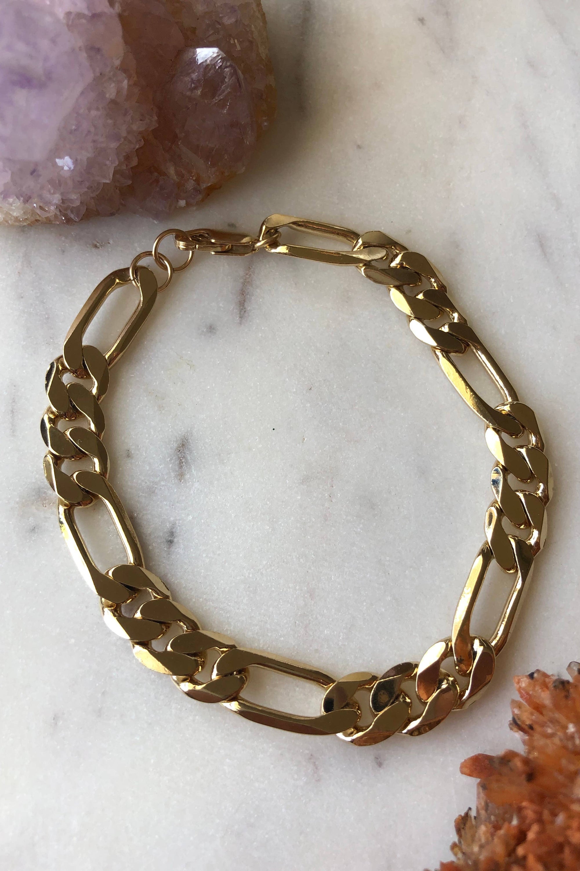 A gold-filled chain bracelet laid out on a marble surface, reflecting light due to its metallic finish.