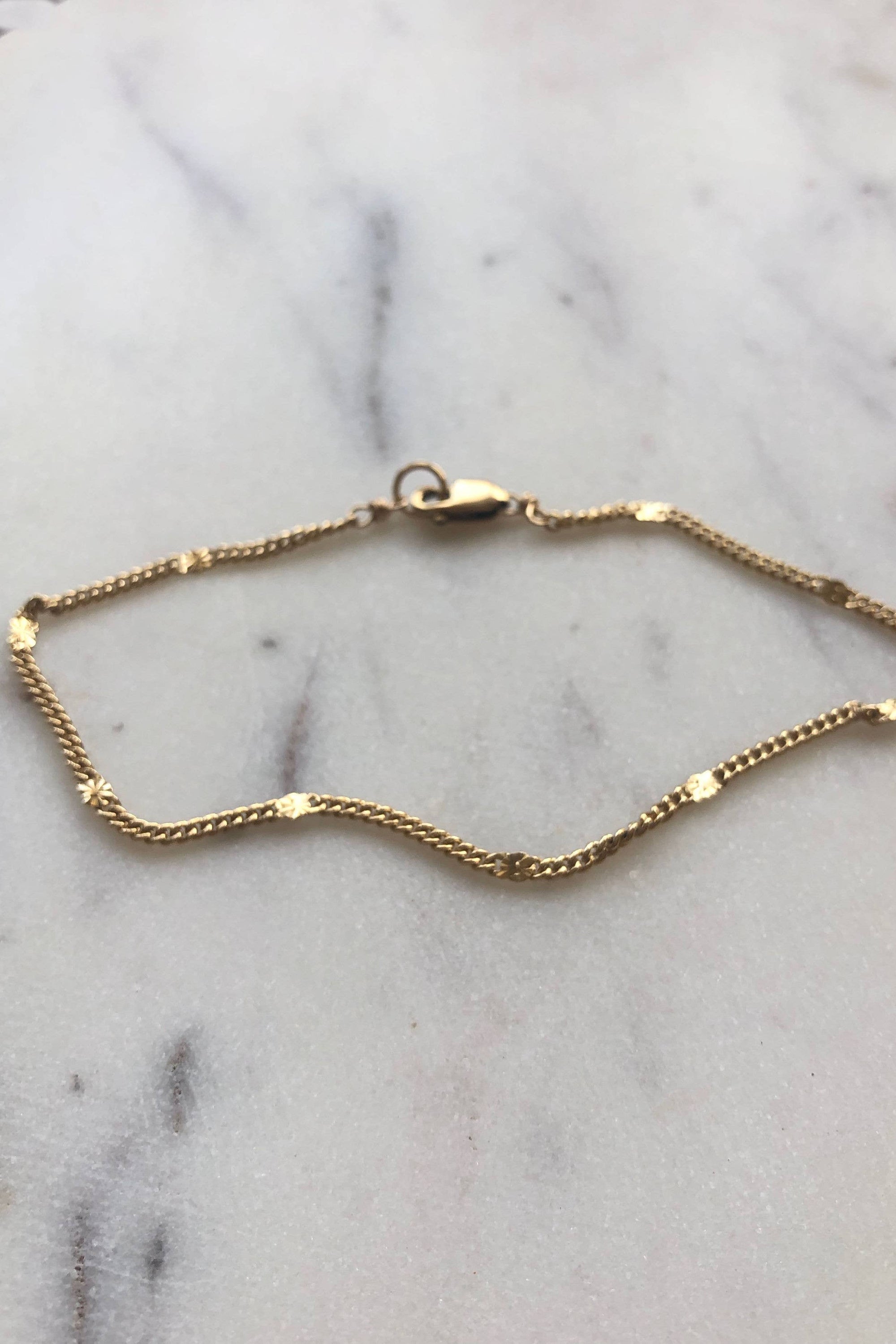 A delicate gold bracelet with a stamped star detail, displayed on a marble surface.