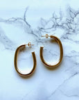 A pair of gold-filled oval thick hoop earrings placed on a marble surface.