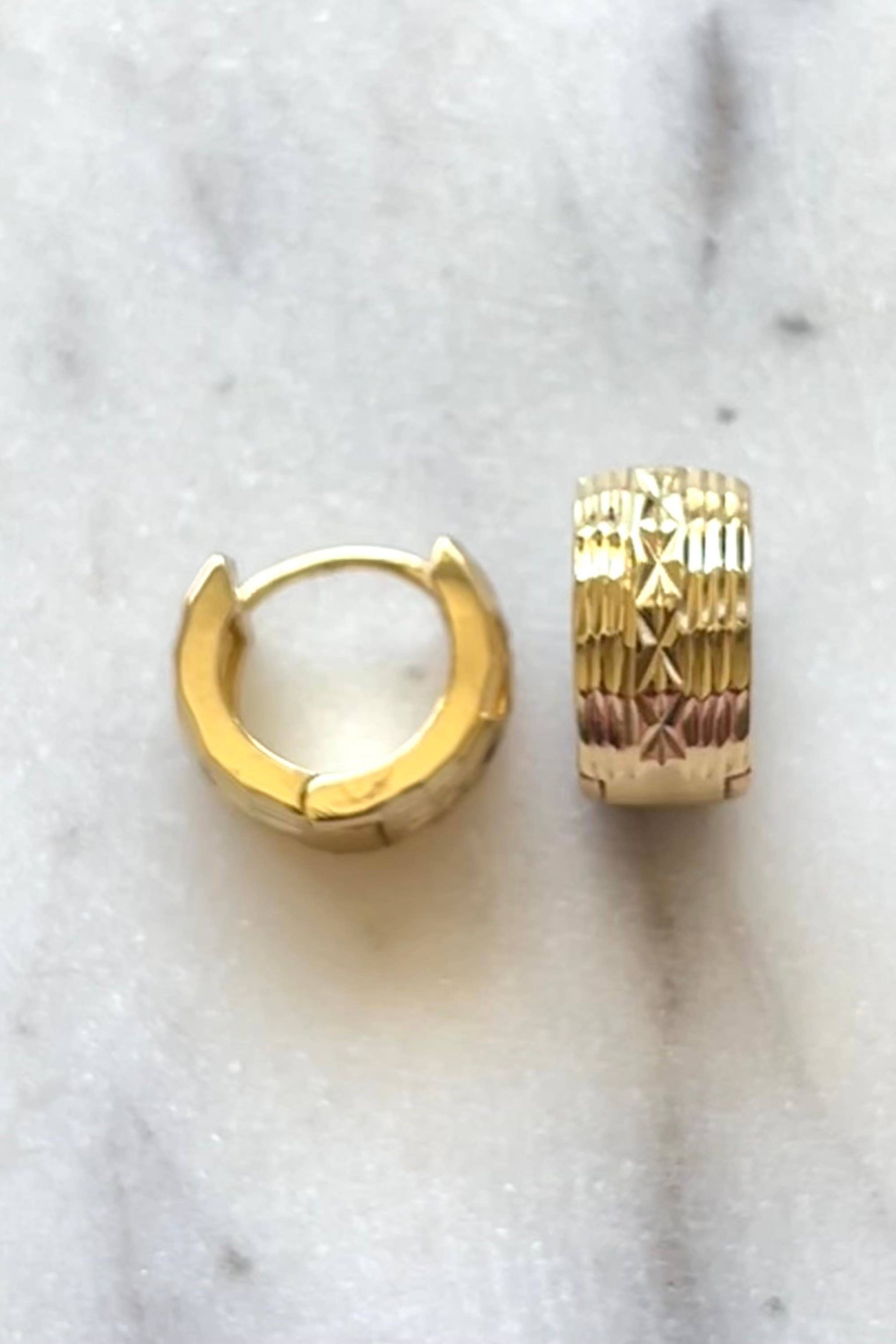 A pair of gold filled huggie hoop earrings with a basketweave texture, displayed on a marble surface.